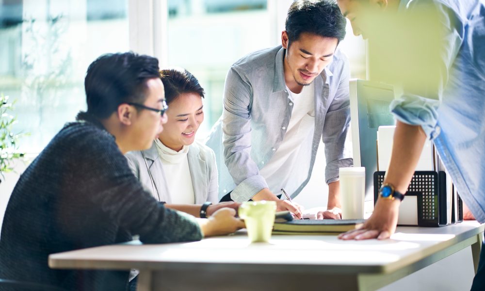 group of four young asian corporate executives meeting in office discussing business in office.